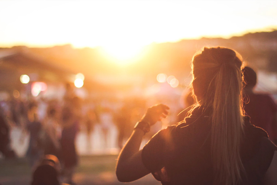 Woman outdoors looks into the sunset across a crowded place.
