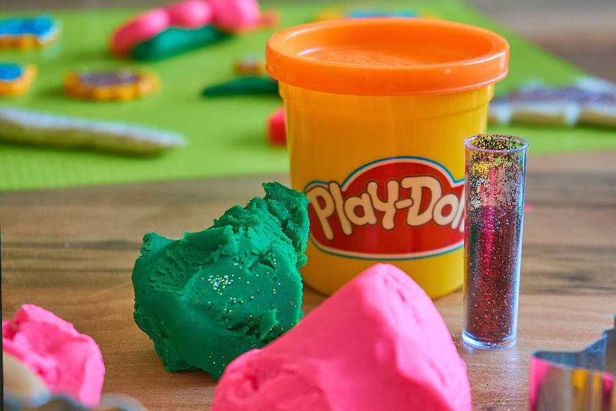 Container labelled Play-Doh with balls of brightly coloured modelling clay for children.