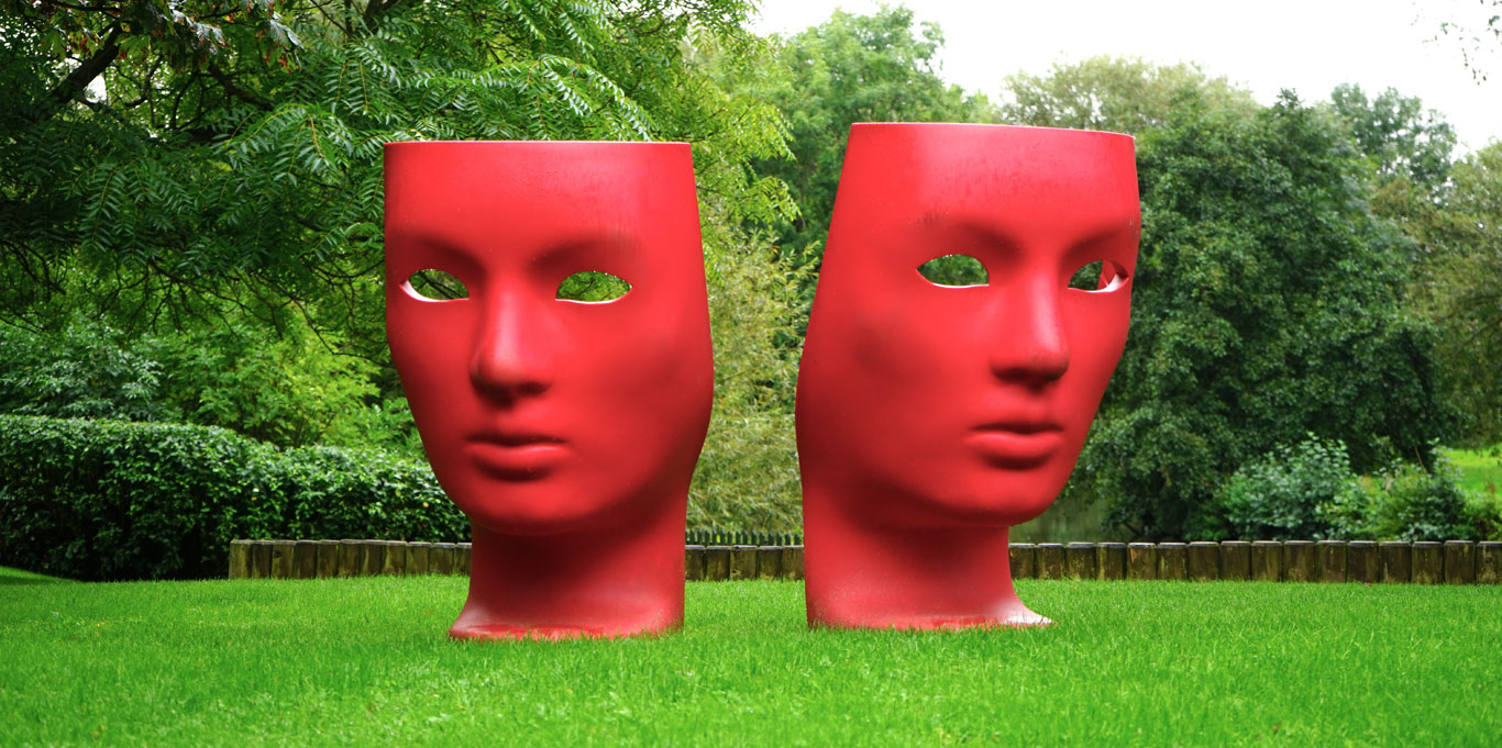 Modern sculpture of two large red masks situated in a garden
