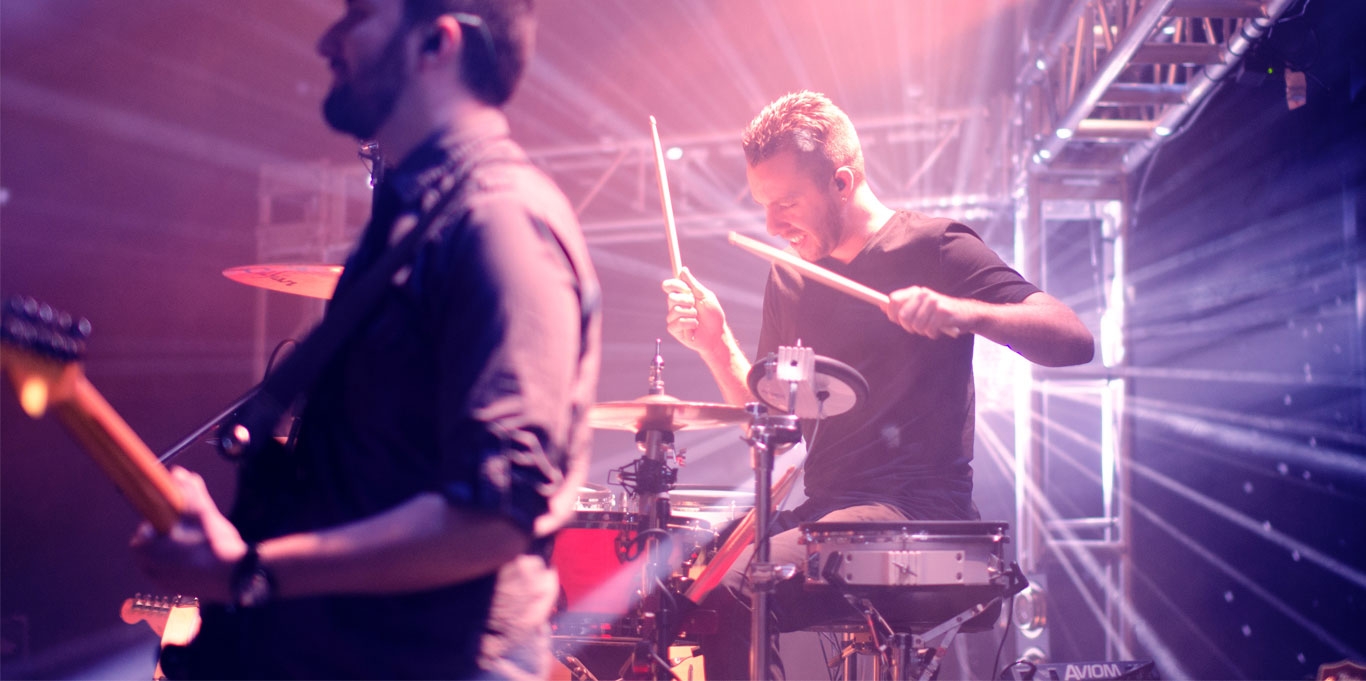 Guitarist and drummer on stage illuminated by orange and blue lighting