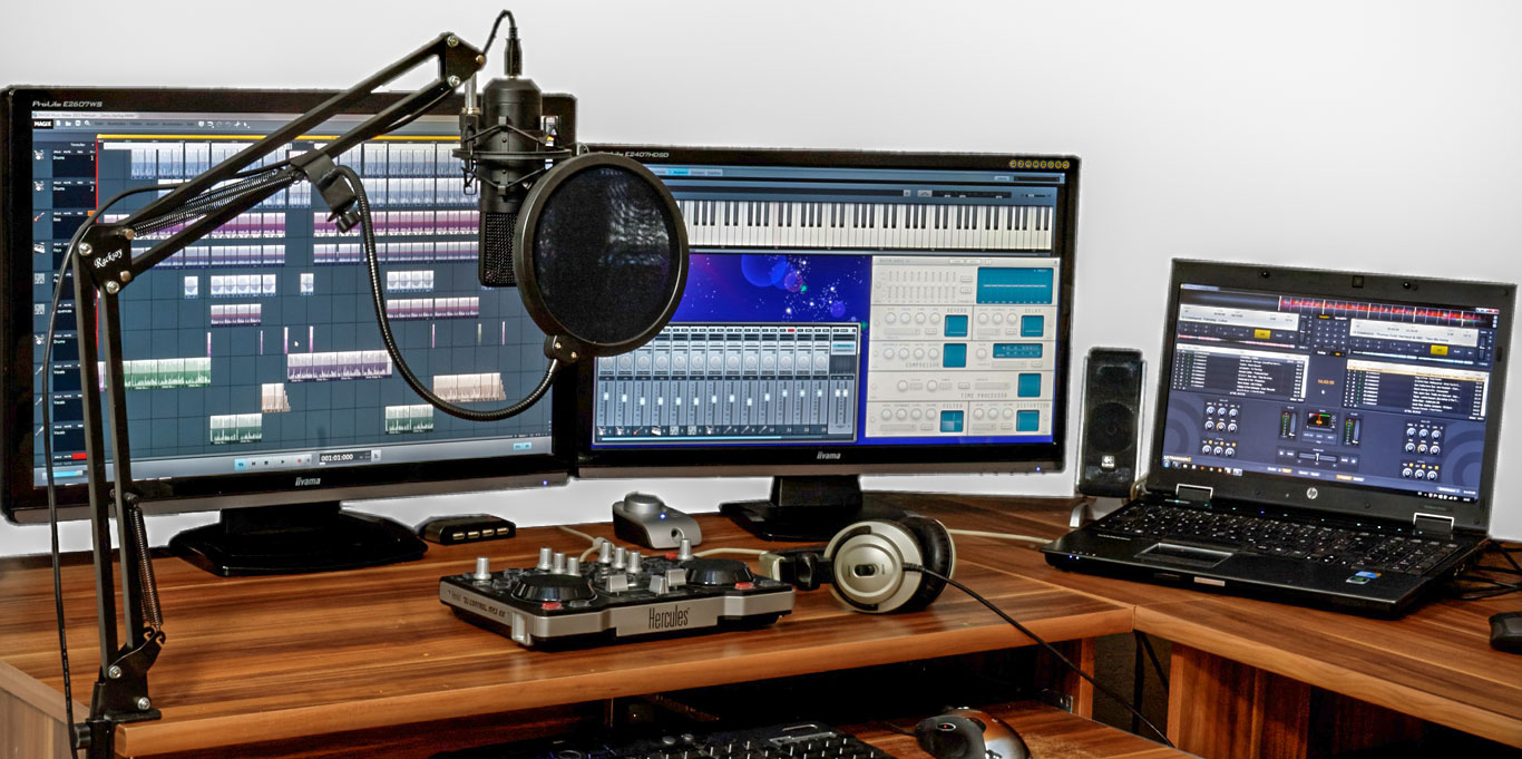 Music editing suite comprising microphone, a computer, two monitors, headphones and small mixing deck.
