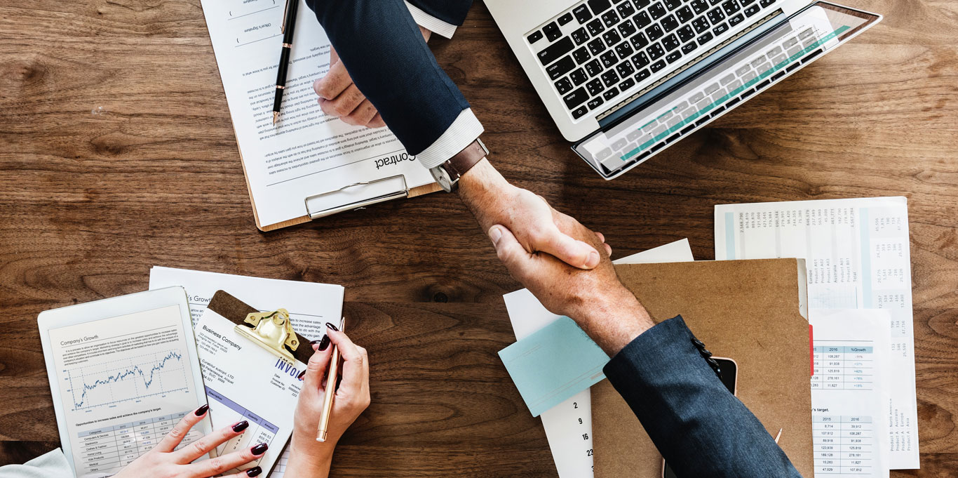 Client shakes the hand of a business person, contracts can be seen on the table