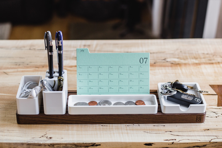 Work desk showing stationery with a calendar and money in tray in front, depicting the concept of time = money.