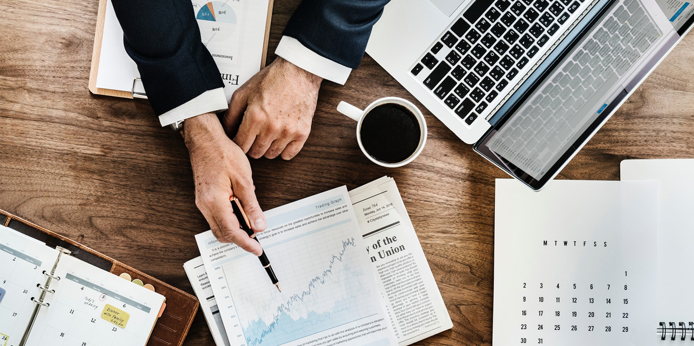 Investor at a table showing computer, spreadsheet, figures and calendar.